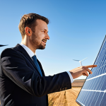 A diverse team of two professional engineers, a man and a woman, both in modest business suits, stand together at a large touchscreen displaying complex schematics of a renewable energy project. In the background, a modern solar farm stretches under a clear sky, symbolizing the transition from theoretical plans to real-world implementation. The scene emphasizes collaboration and problem-solving, with one person pointing to a detail on the screen and the other holding a tablet with data. Perfect anatomy, correct proportions, natural pose, well-formed hands, proper finger count, natural body proportions. Fully clothed, appropriate attire, professional dress, safe for work, appropriate content, family-friendly, high quality professional photography, crisp focus, vibrant colors.